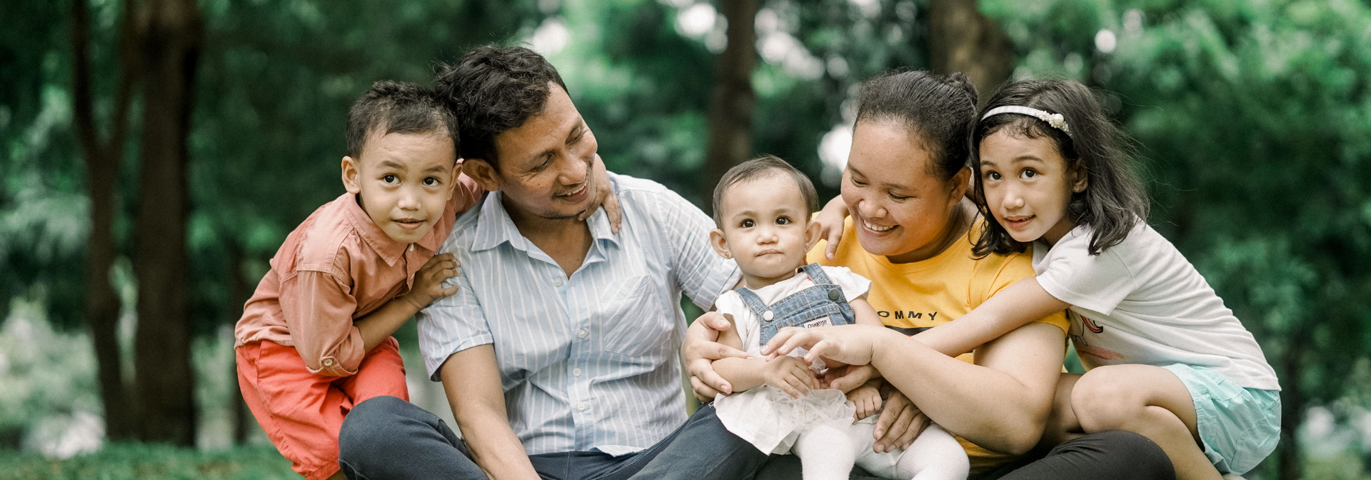 Family lying on grass together outdoors, smiling and holding two babies.