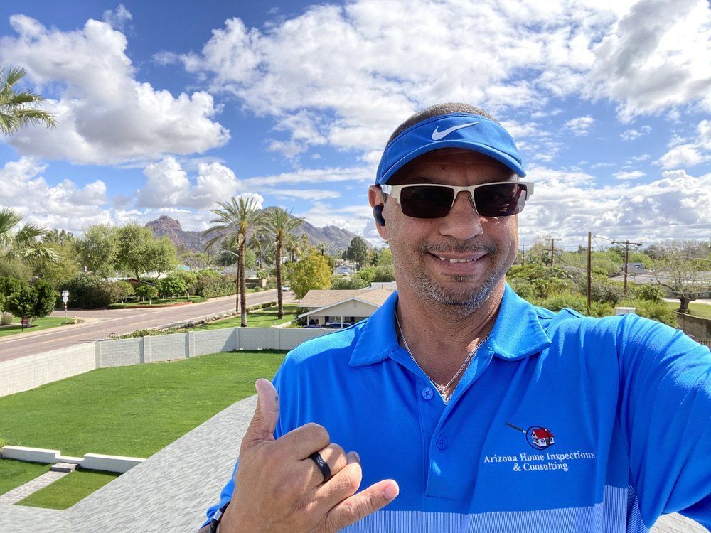 A man wearing sunglasses and a blue shirt is giving a thumbs up.