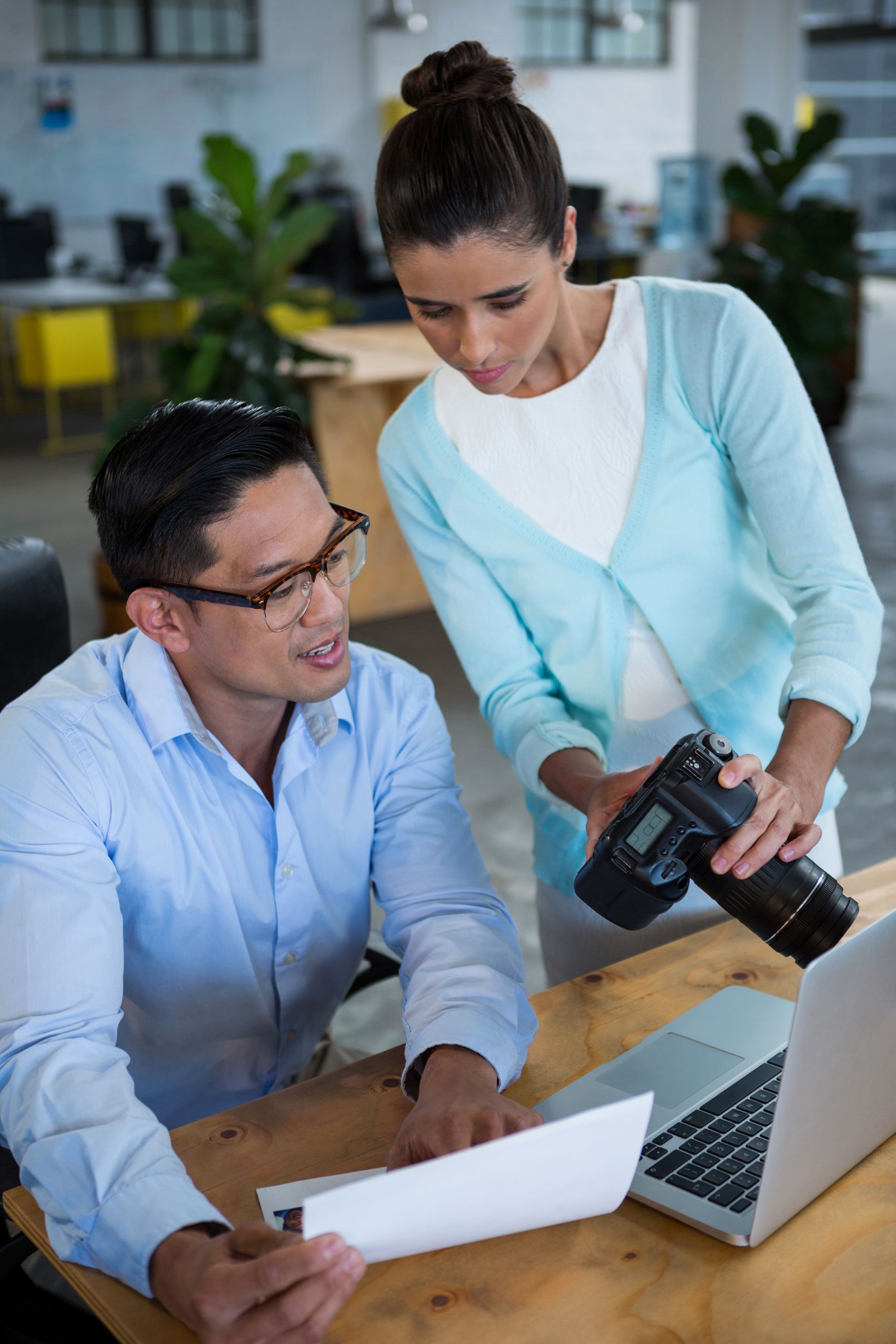 A man and a woman are looking at a laptop and a camera.