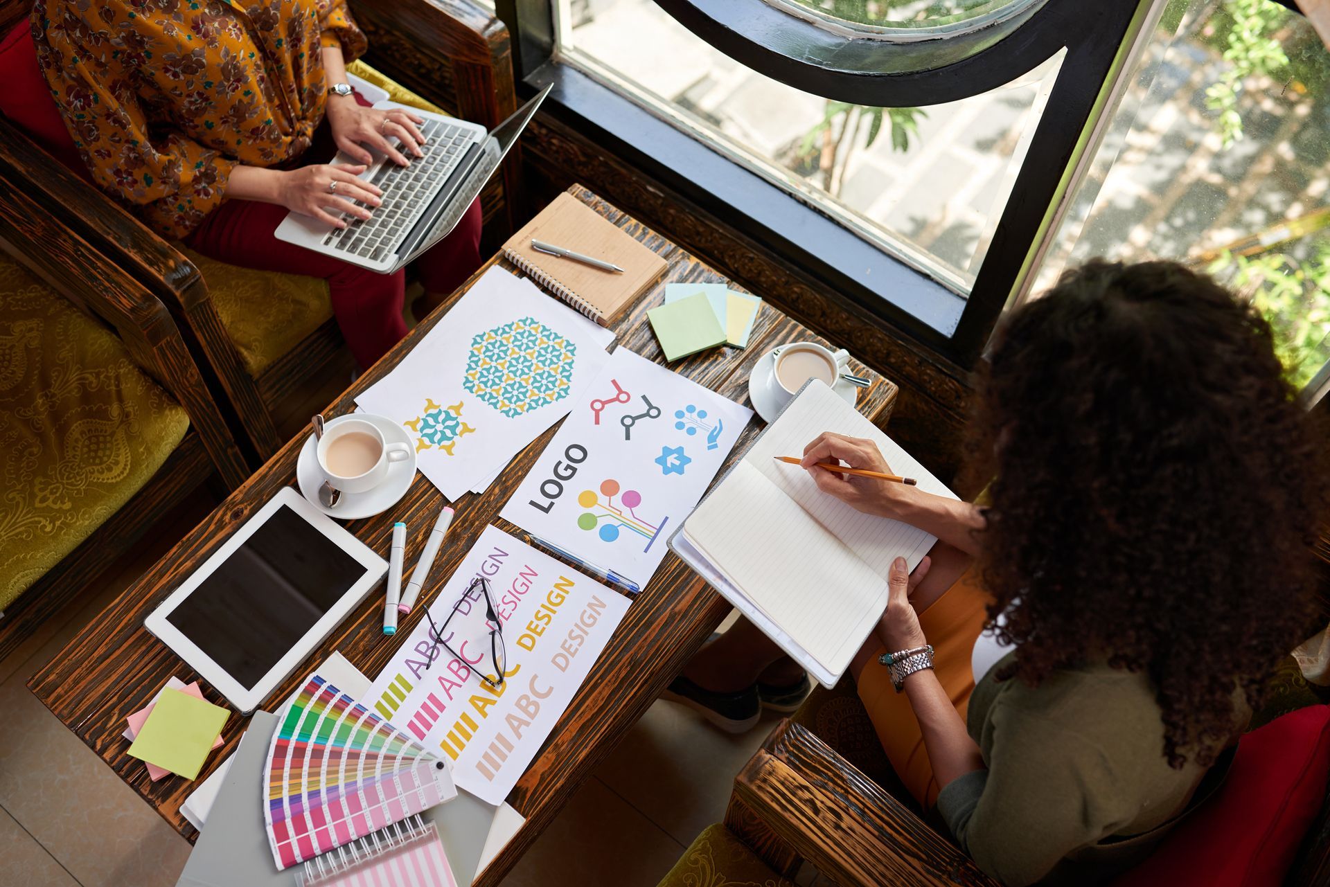 Two women are sitting at a table with a laptop and a tablet.