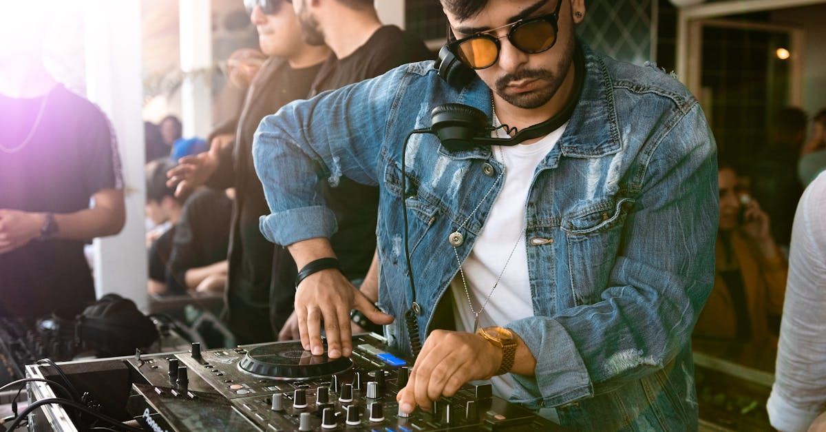 A man in a denim jacket is playing music on a mixer at a party.