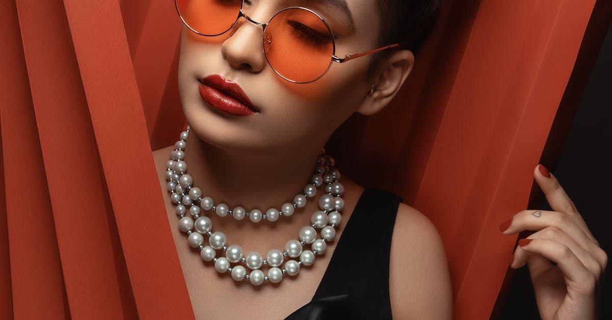A woman wearing a pearl necklace and sunglasses is standing in front of a red curtain.