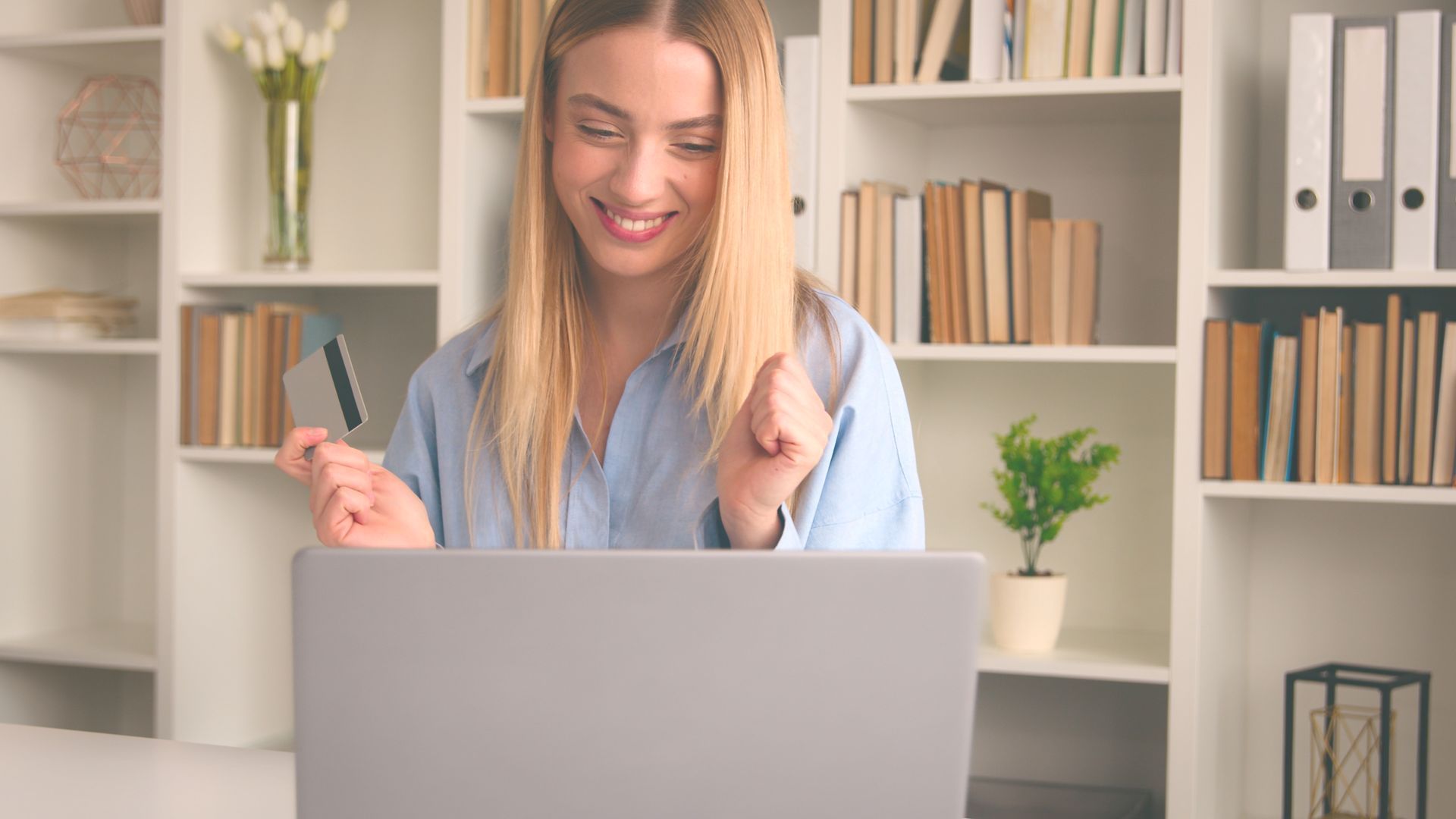 A woman is sitting in front of a laptop computer holding a credit card.