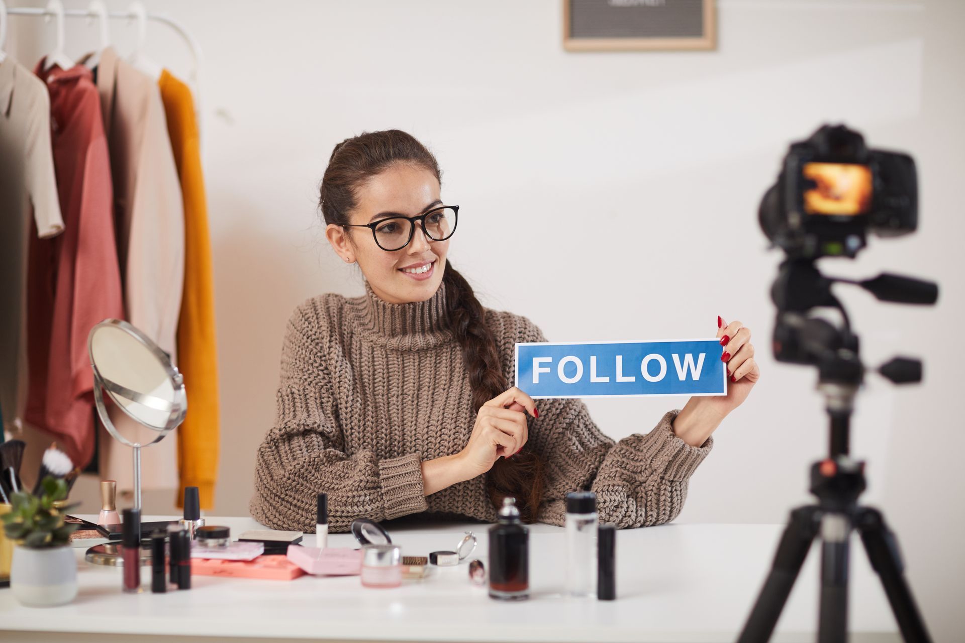 A woman is holding a sign that says follow in front of a camera.