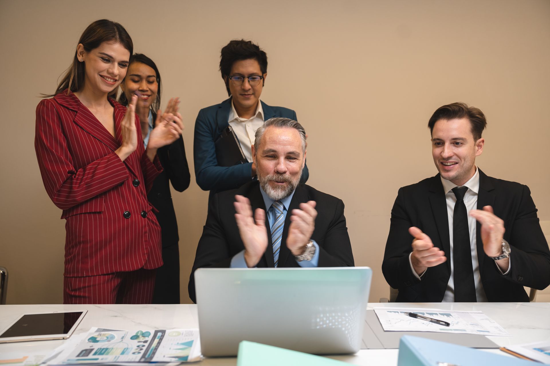 A group of people are clapping in front of a laptop computer.