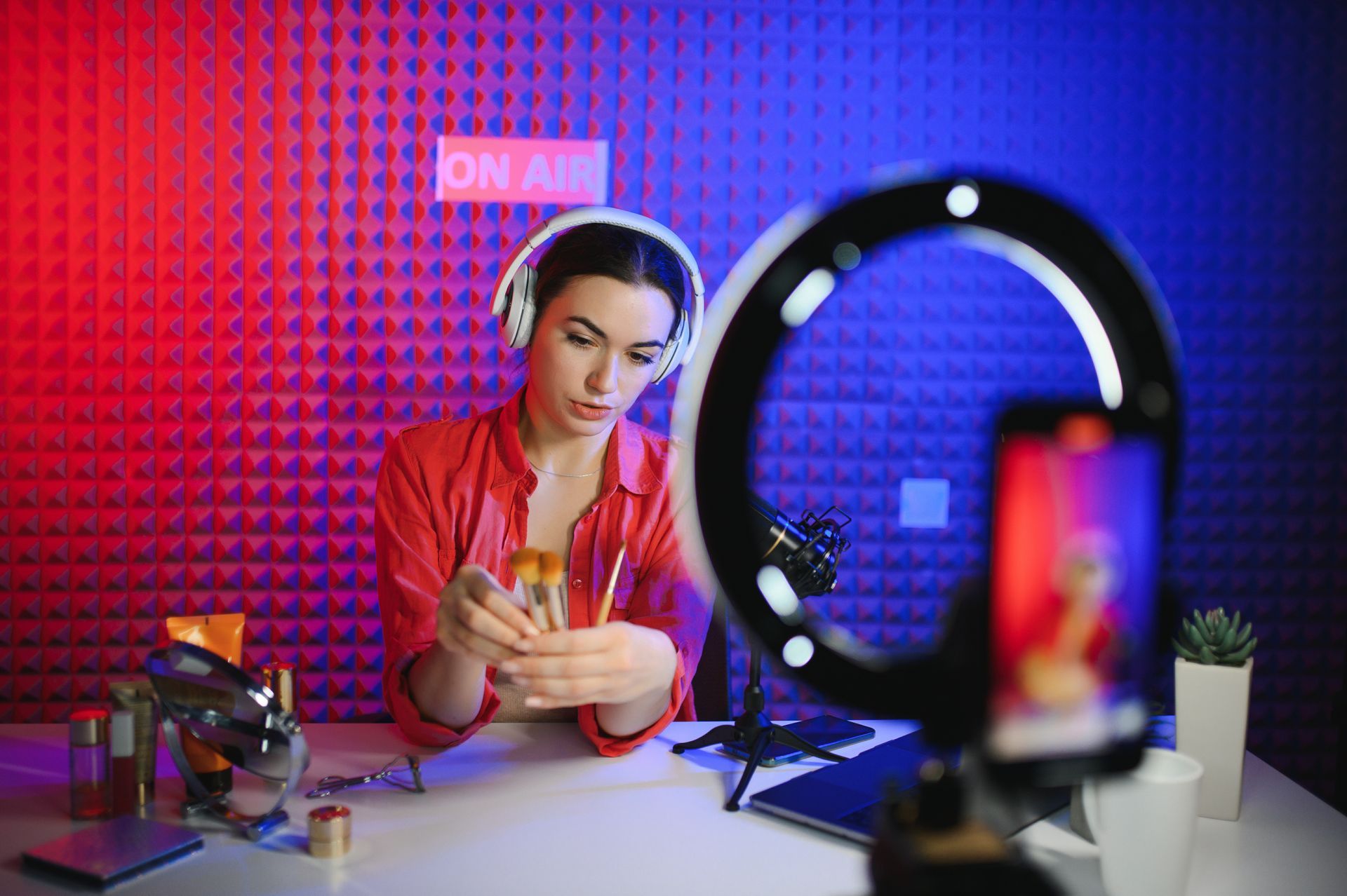 A woman is wearing headphones and using a cell phone in front of a ring light.