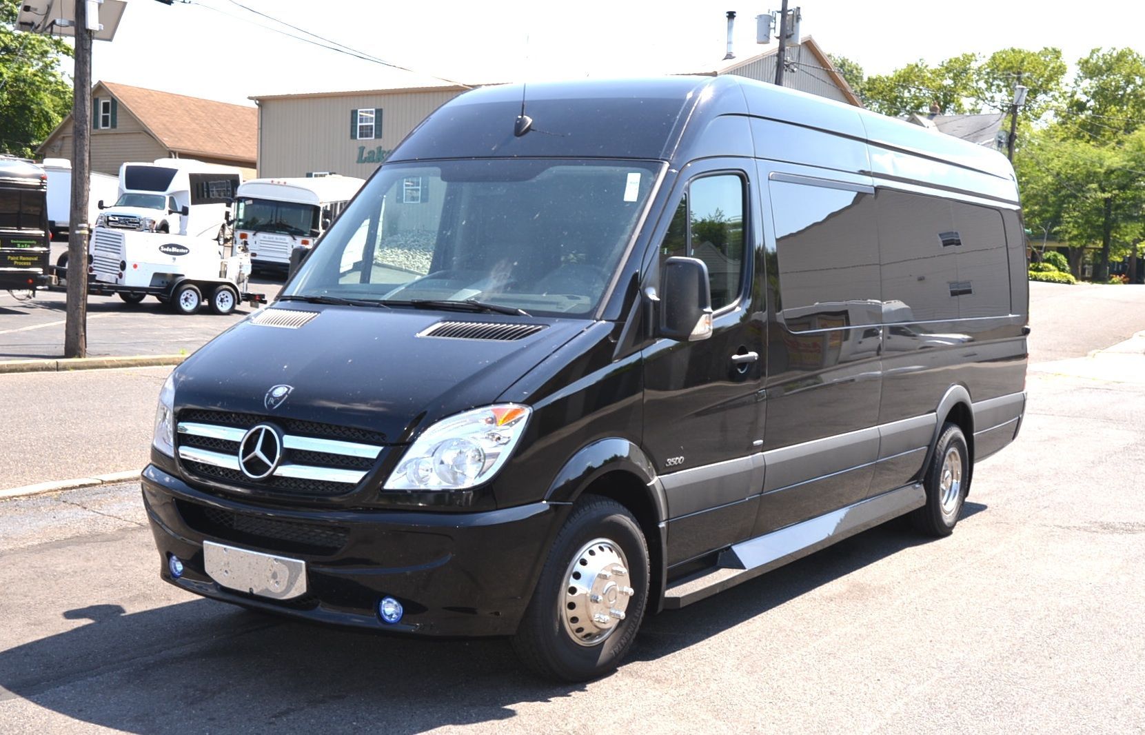 Black Mercedes Sprinter van parked in a lot, with buildings in the background.