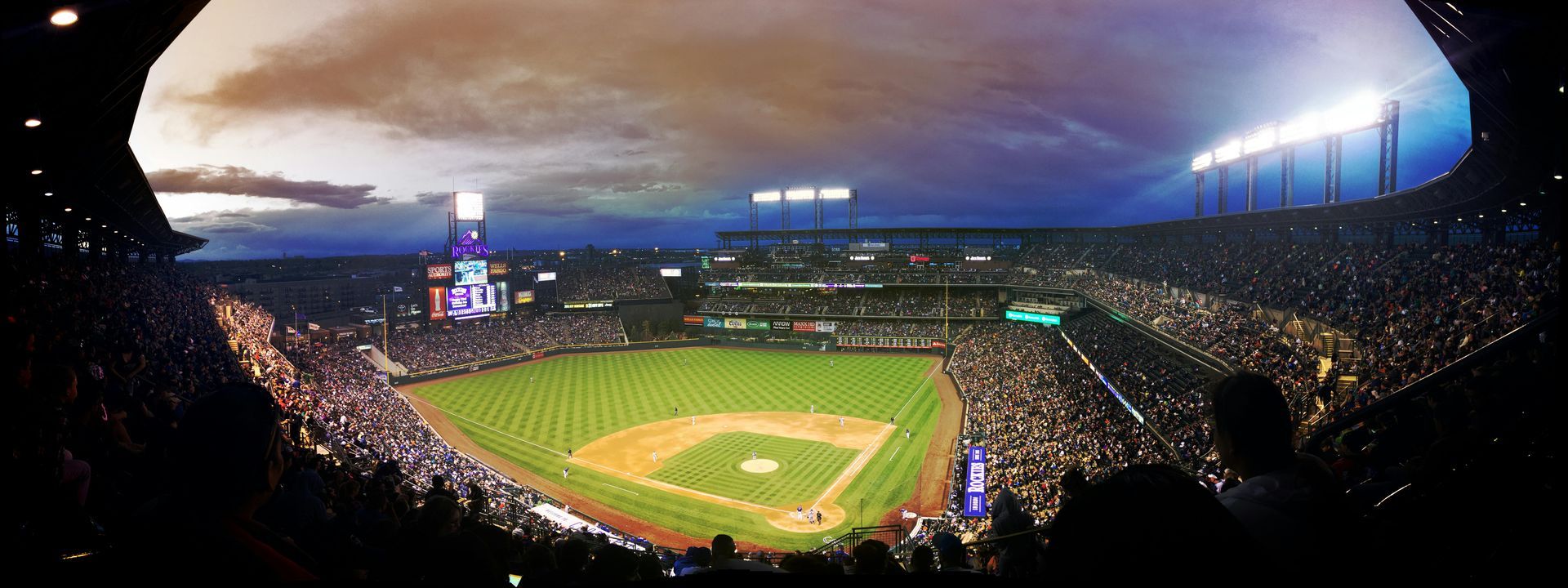 Baseball stadium at dusk, filled with fans, illuminated by bright lights.