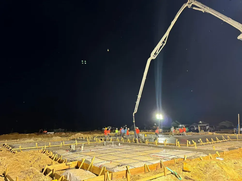 A concrete pump is pouring concrete on a construction site at night.