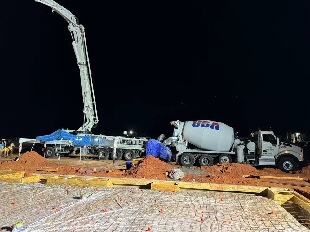 A concrete mixer truck is pouring concrete on a construction site at night.