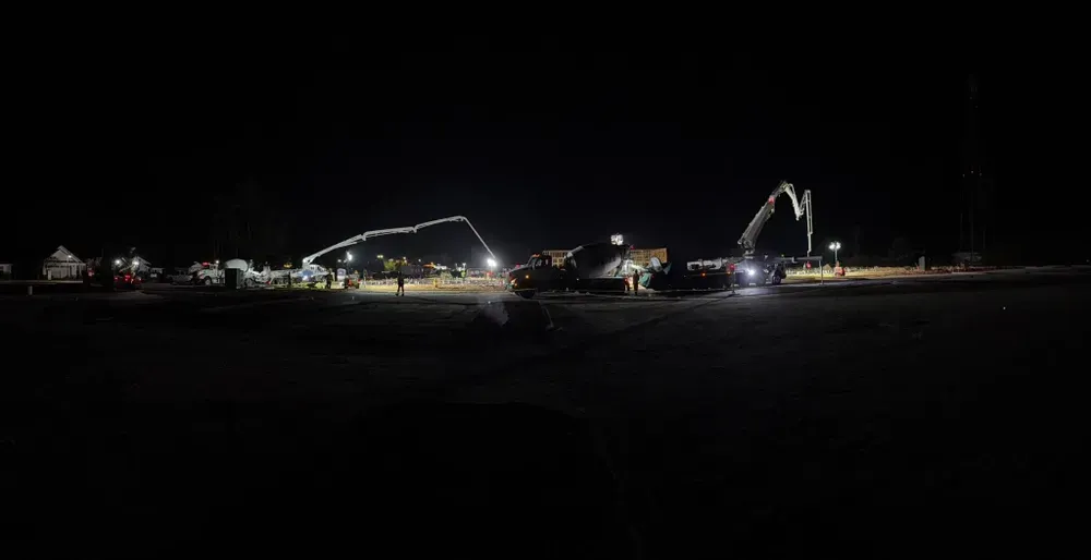 A group of construction vehicles are working on a construction site at night.