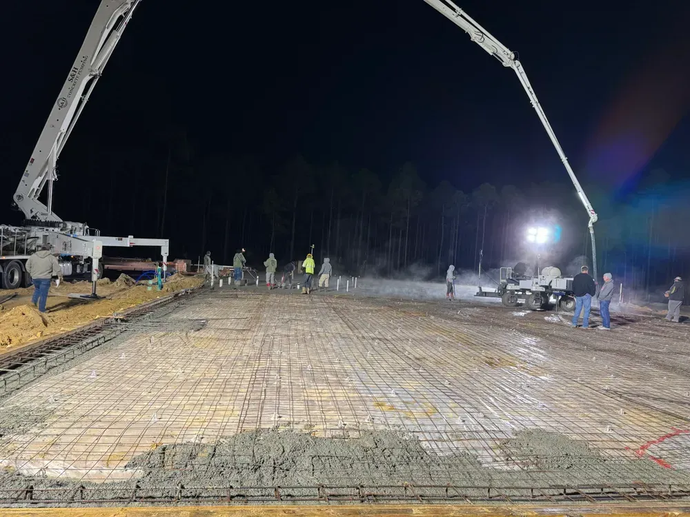 A concrete pump is pouring concrete on a construction site at night.