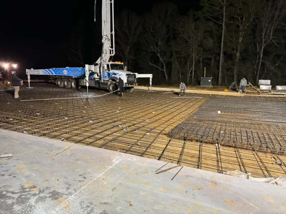 A truck is pumping concrete into a concrete floor at night.