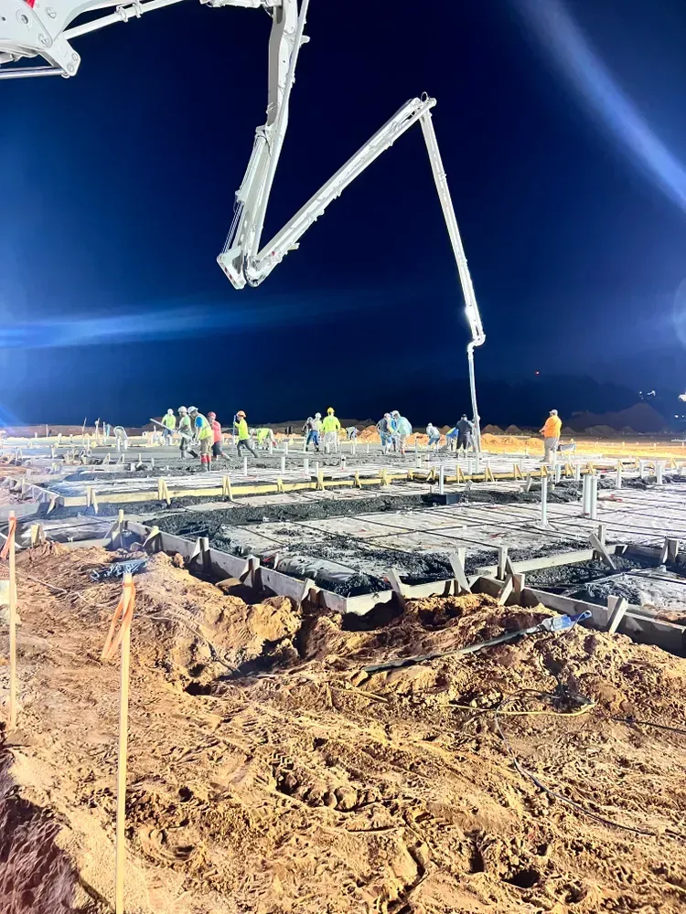 A concrete pump is pouring concrete on a construction site at night.