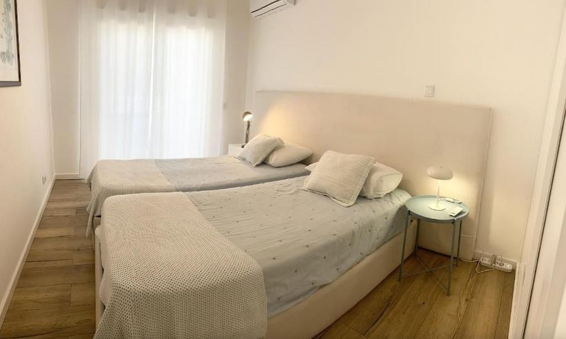 A bedroom with two beds, bedside table and window.