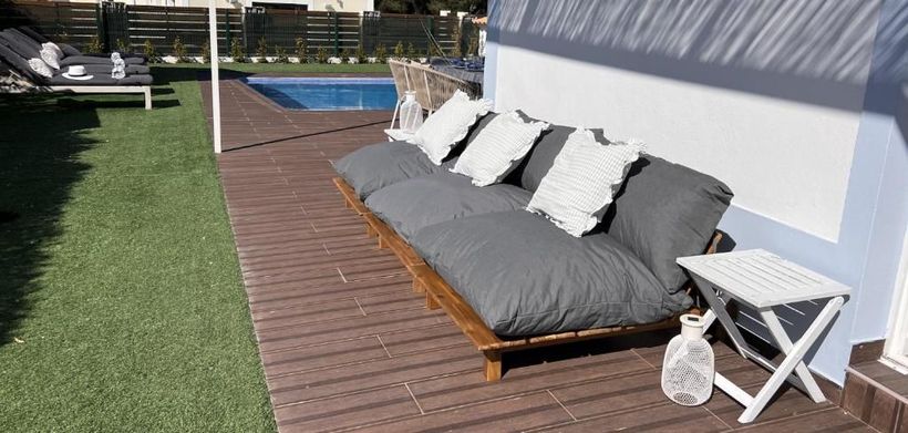 Um sofá está sentado em um deck de madeira ao lado de uma piscina.