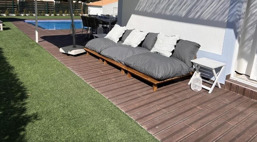 A sofa sits on a wooden deck next to a swimming pool.