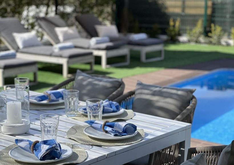 A table with plates and glasses in front of a swimming pool.