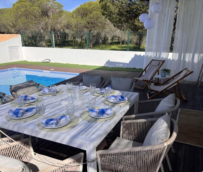 A table with plates and glasses in front of a swimming pool.