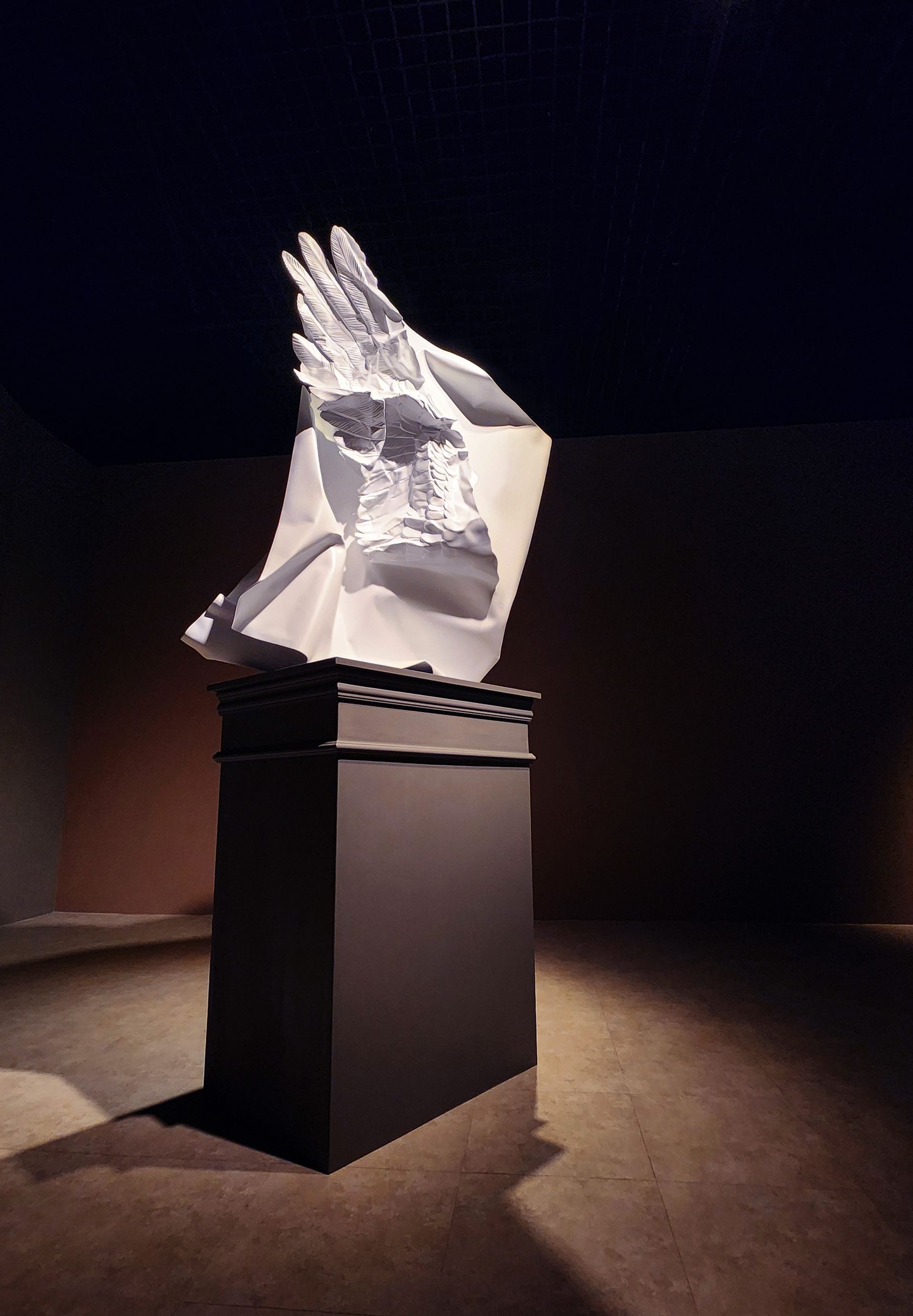 A statue of a bird is sitting on a black pedestal in a dark room.