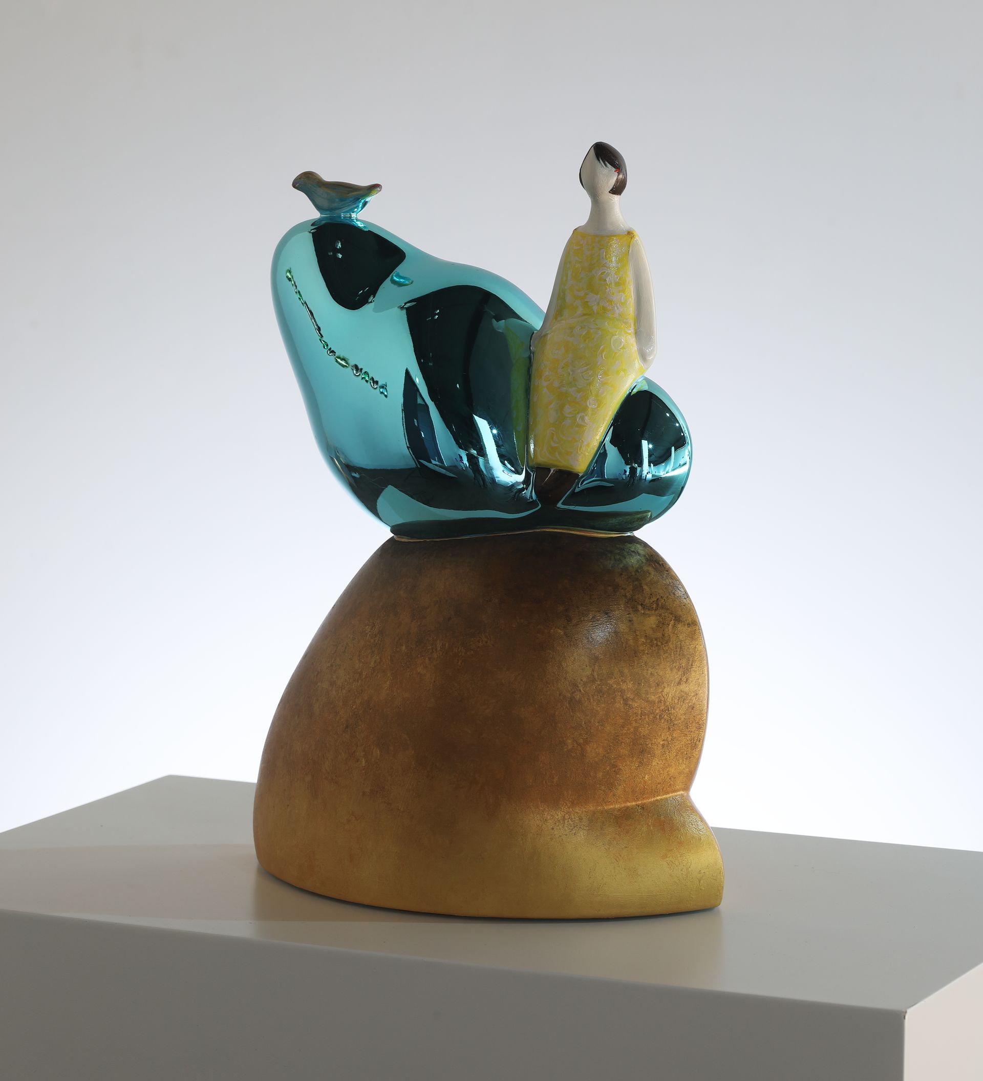 A statue of a woman in a yellow dress sitting on a blue object