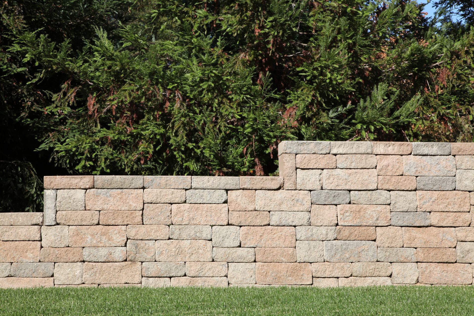 Stone retaining wall with green shrubs in background.
