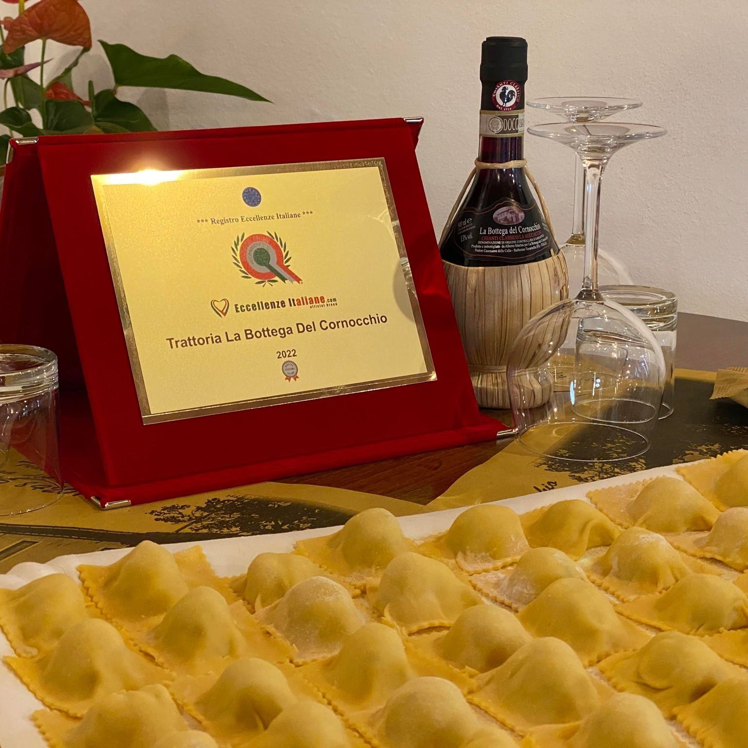 Ravioli su un vassoio vicino a una targa di premiazione e una bottiglia di vino sul tavolo.