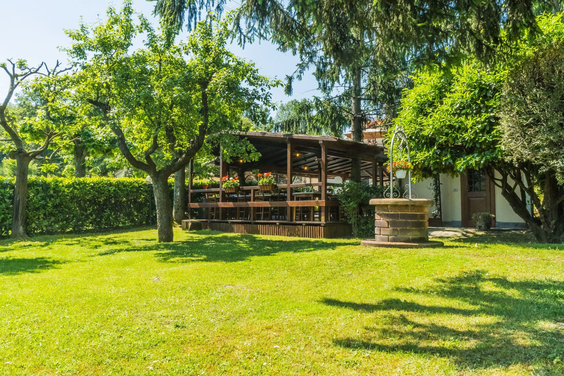 Giardino verdeggiante con gazebo e pozzo in piena luce solare.
