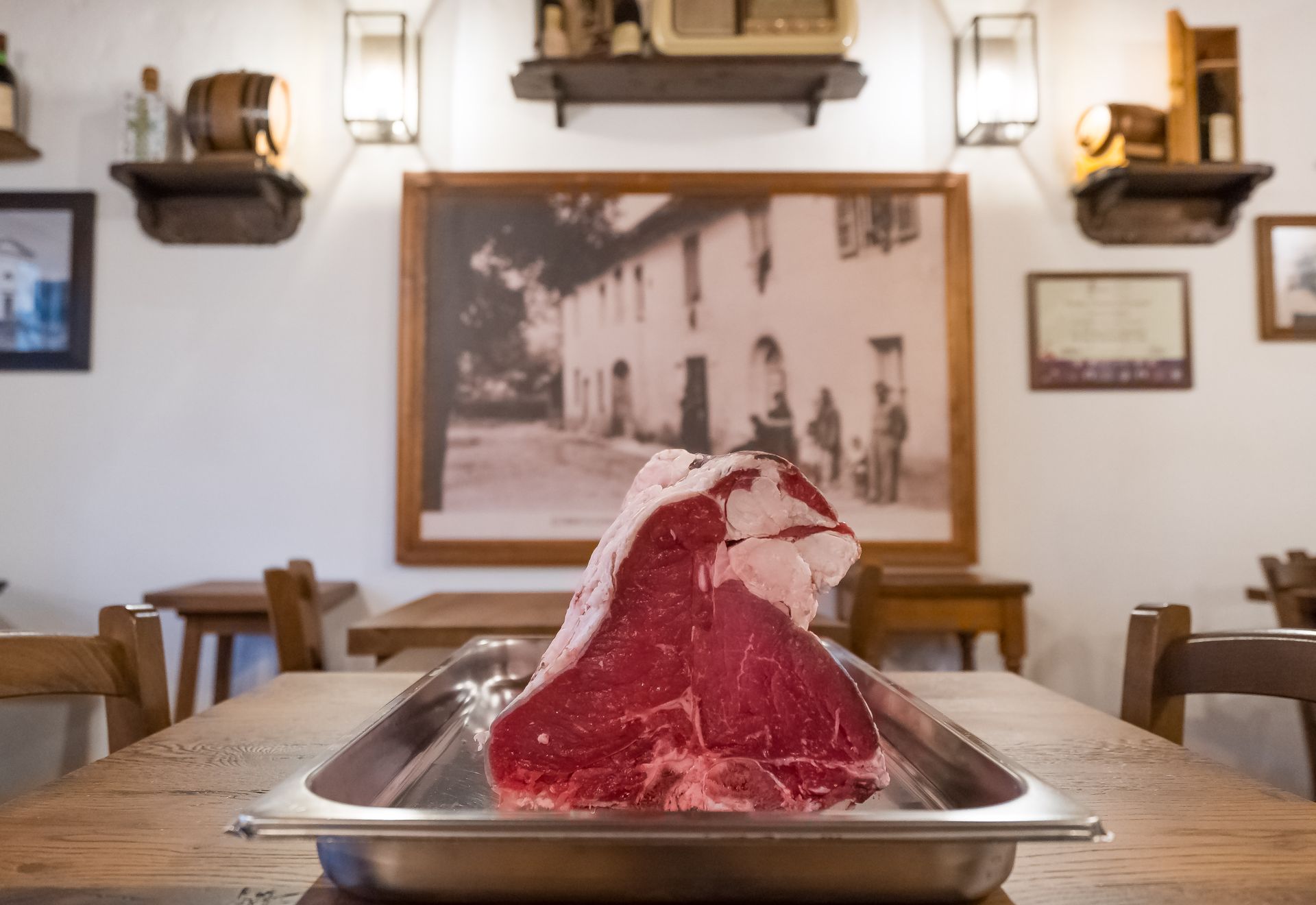 Una grande bistecca cruda su un vassoio di metallo appoggiato su un tavolo di legno in un ristorante.