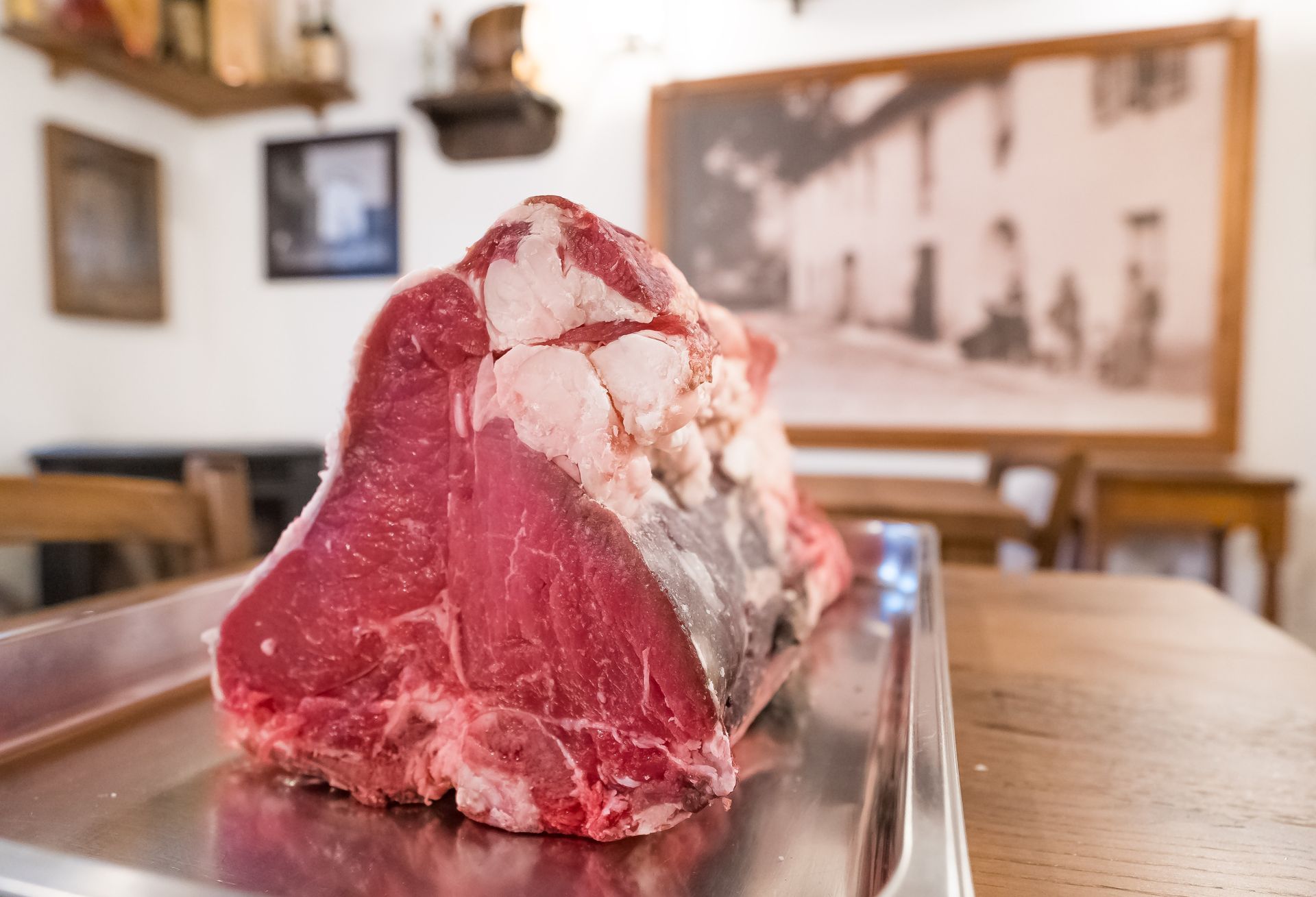Una grande bistecca cruda su un vassoio d'argento, in un ambiente da ristorante.