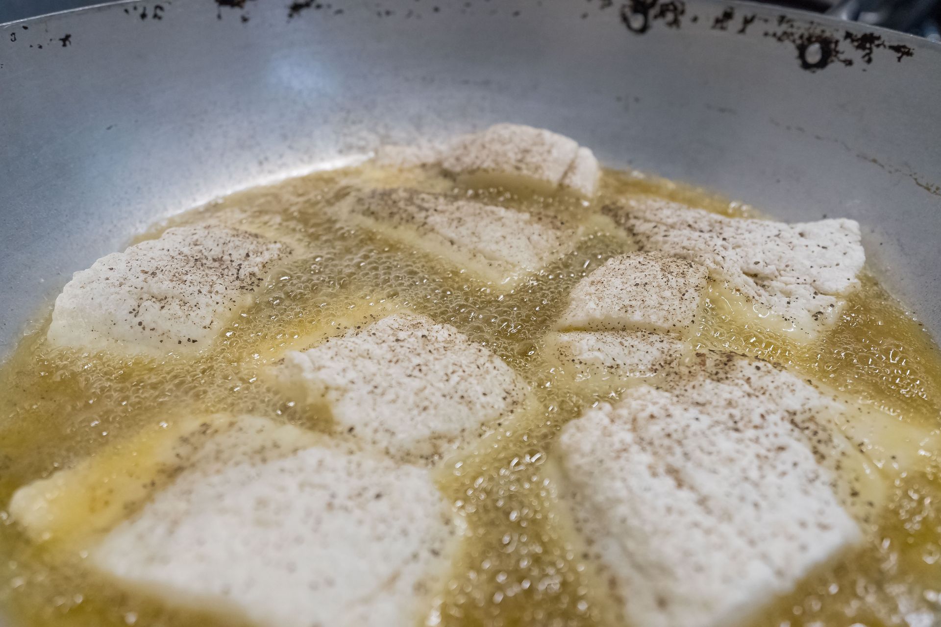 Filetti di pesce fritti in padella con olio caldo. Pesce chiaro condito con pepe nero.