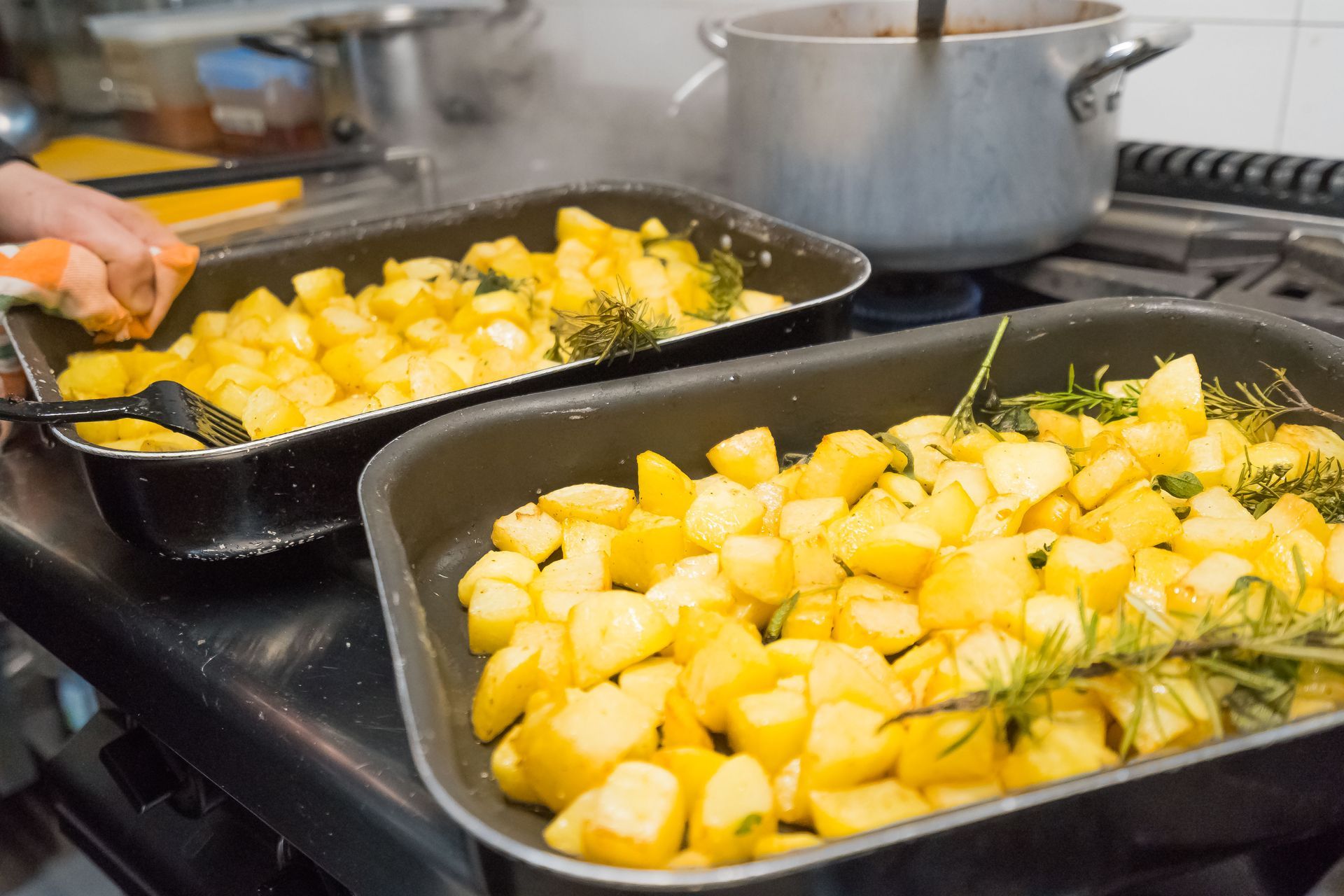 Patate arrostite in due teglie nere, cottura a vapore, impostazione della cucina.