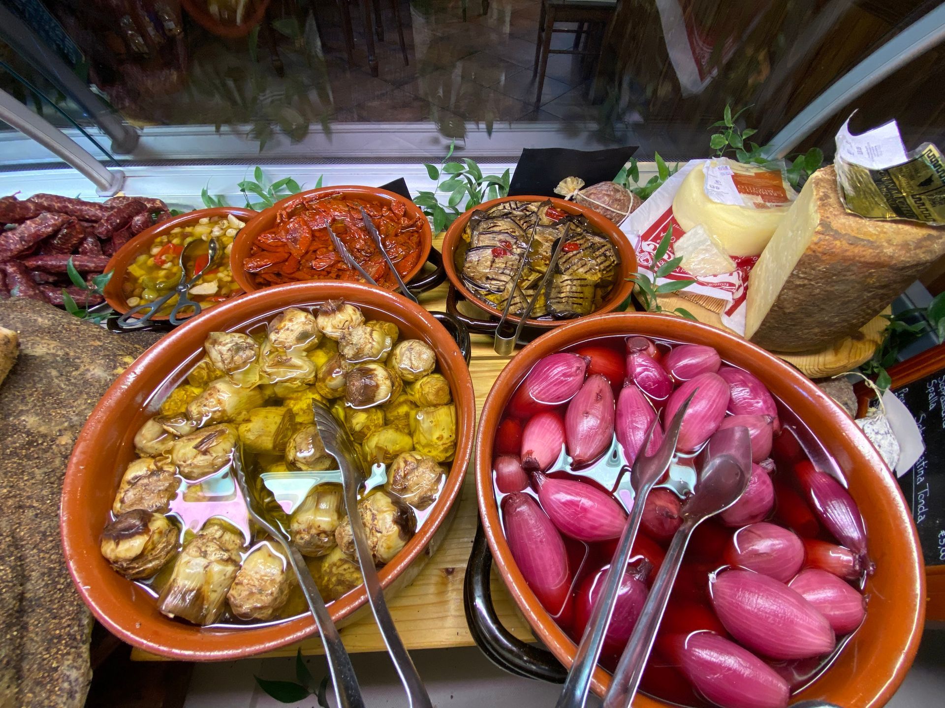 Esposizione di varie verdure sottaceto in ciotole di terracotta, tra cui funghi, cipolle e pomodori.