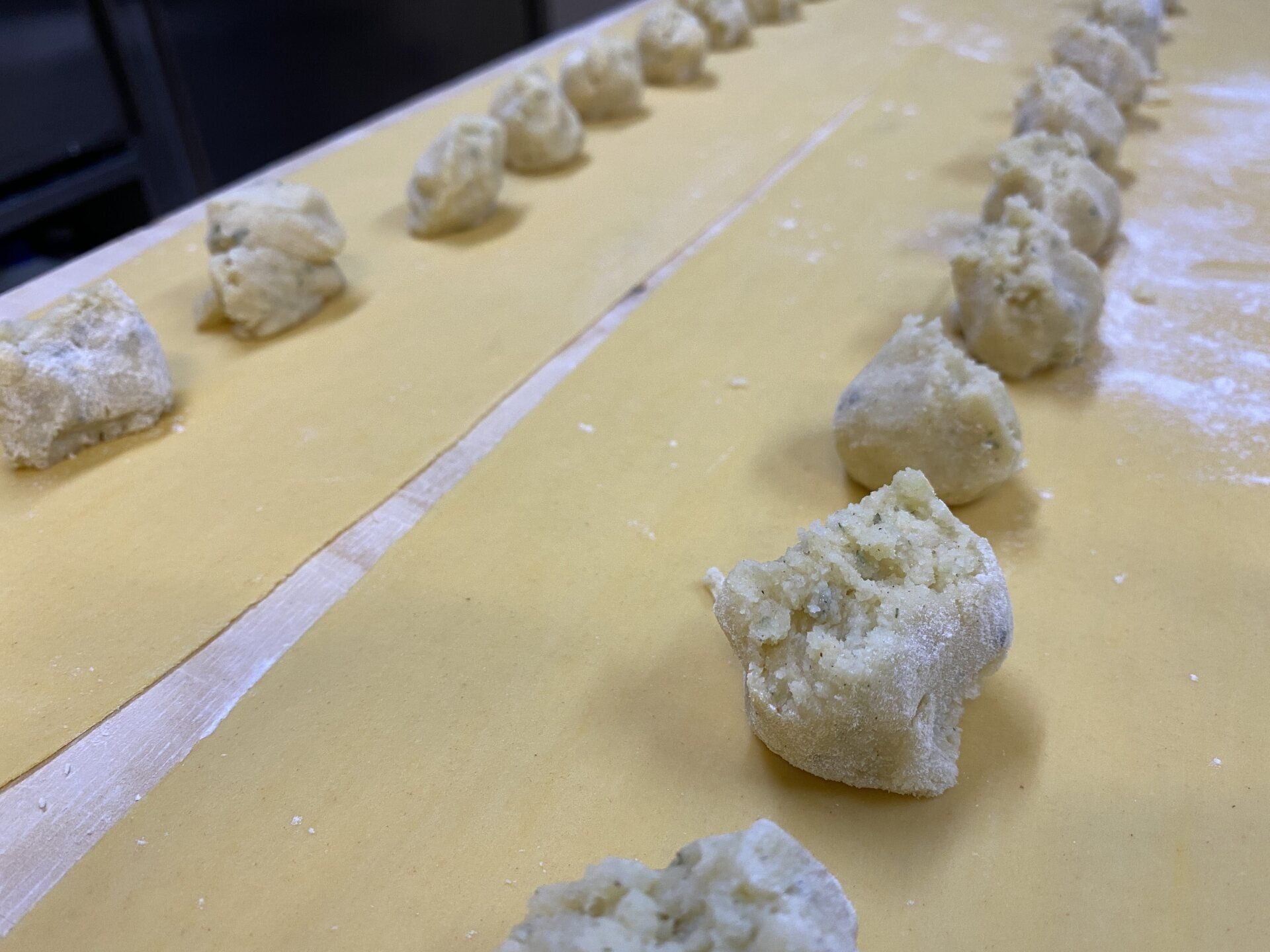 File di palline di pasta su sfoglie di pasta gialla piatte, pronte per i ravioli.