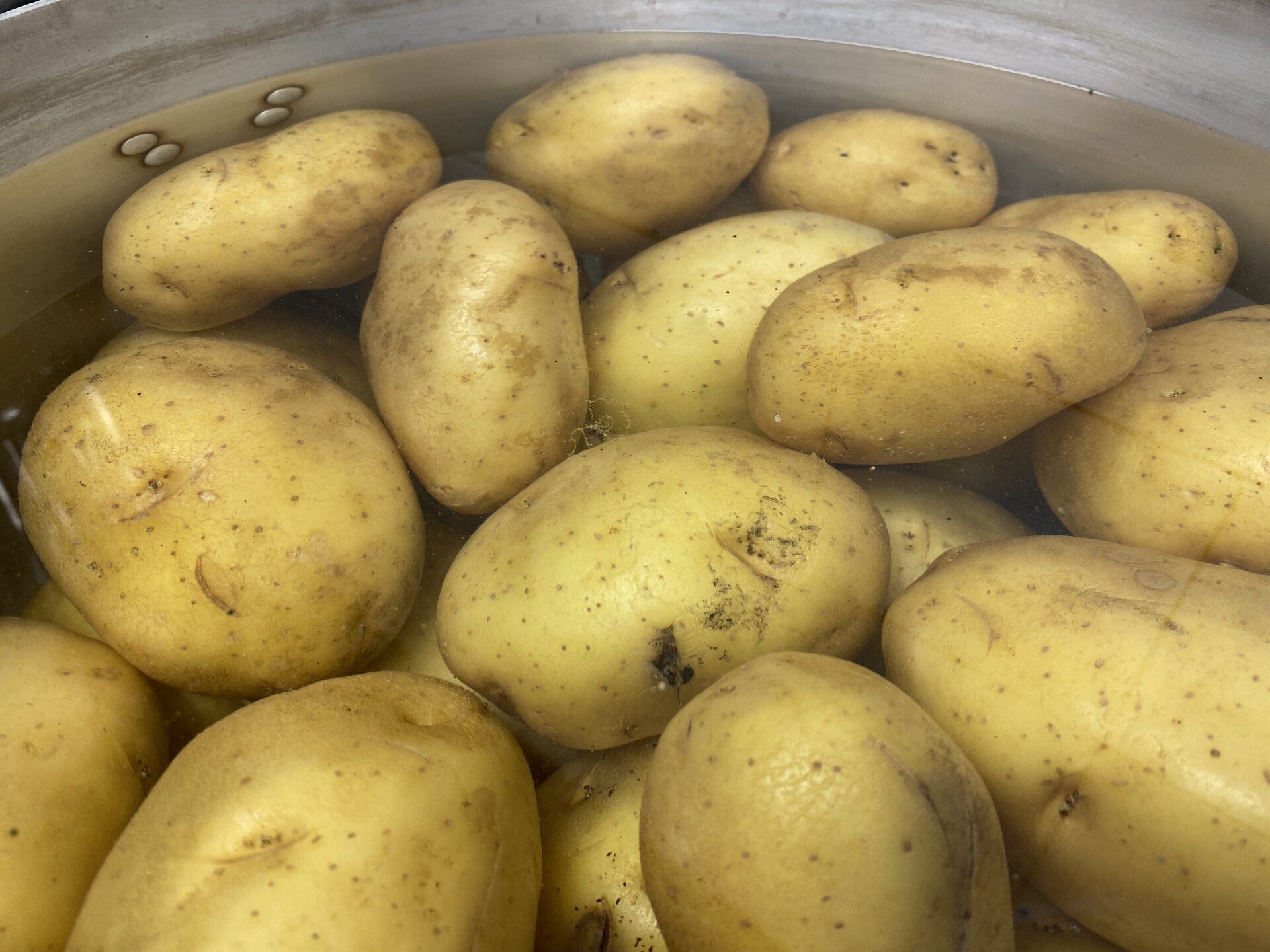 Patate che bollono in una pentola di metallo, con l'acqua visibile.
