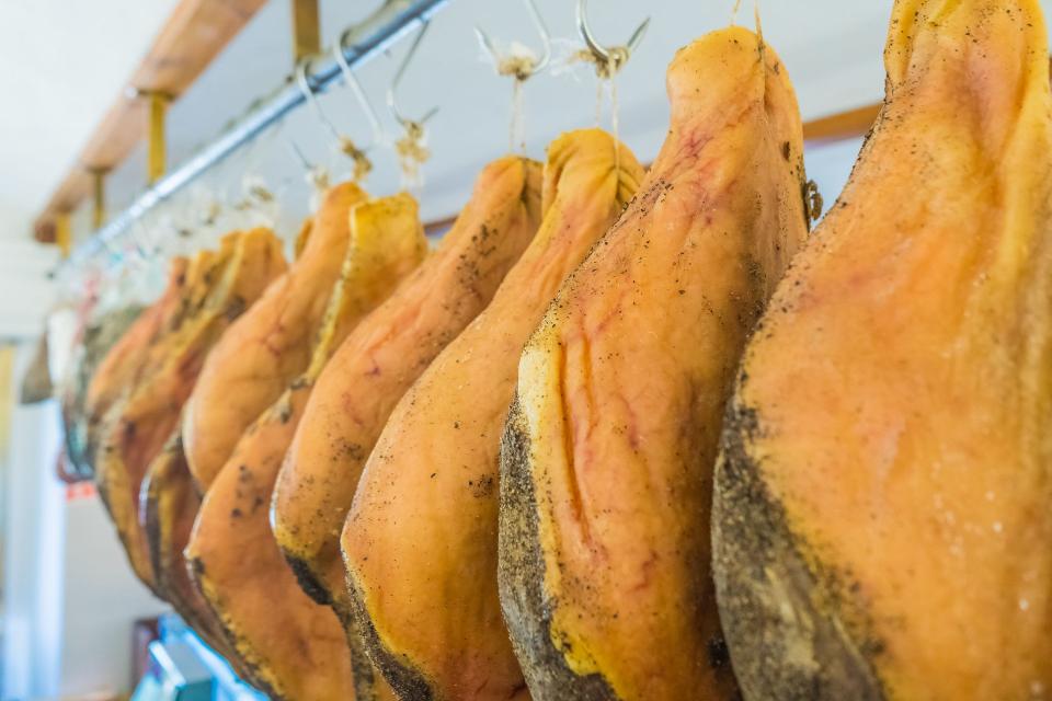 Cosce di prosciutto stagionato appese a un'asta di metallo in un locale di stagionatura.
