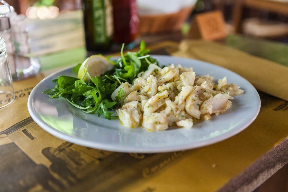 Piatto di cibo con pesce e rucola, spicchio di lime, servito su una tovaglia gialla a fantasia.