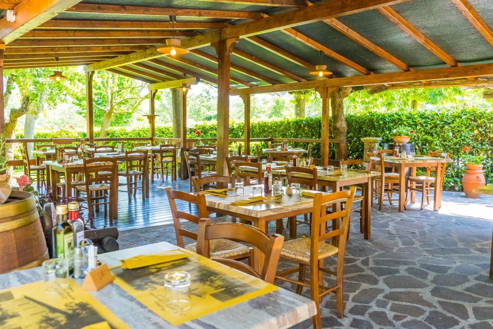 Ristorante all'aperto con tavoli e sedie in legno sotto un patio coperto.