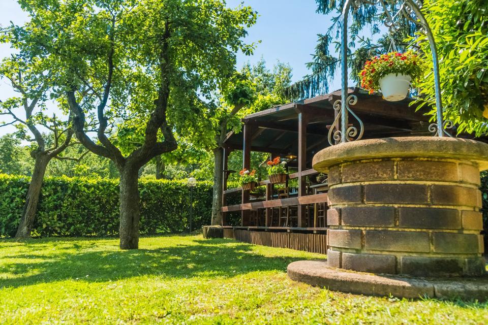 Pozzo in pietra e gazebo in legno in un giardino verde e soleggiato.