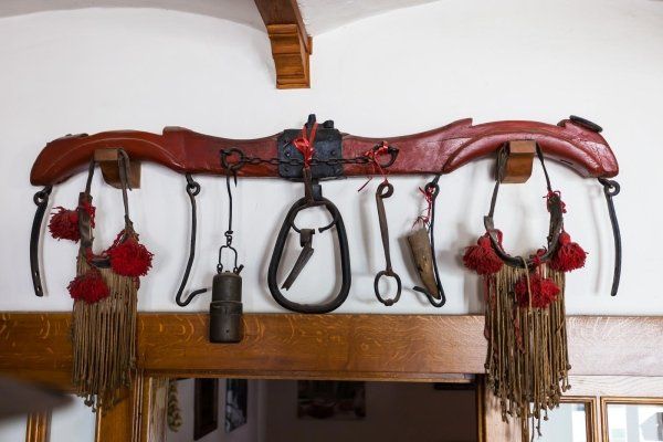 Decorazione murale in legno con nappe rosse, campanelli e utensili in metallo forgiato appesi sopra una porta.