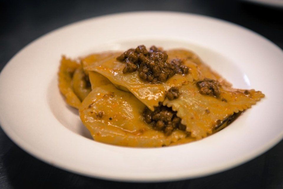 Ravioli di pasta conditi con sugo di carne marrone scuro in una ciotola bianca.