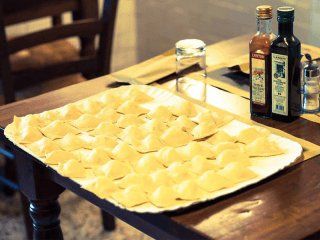 Un vassoio di ravioli crudi su un tavolo di legno, con bottiglie di olio e aceto.