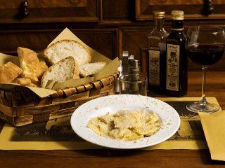 Piatto di ravioli, cestino del pane, olio d'oliva, bicchiere di vino sul tavolo.