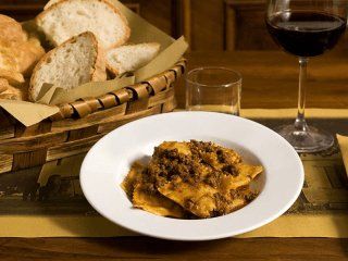 Piatto di pasta con sugo di carne, cestino del pane, bicchiere d'acqua e bicchiere di vino su un tavolo di legno.