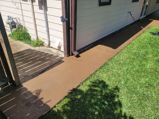 Side yard beside a house with a brown walkway, green grass, and a wooden fence in sunlight