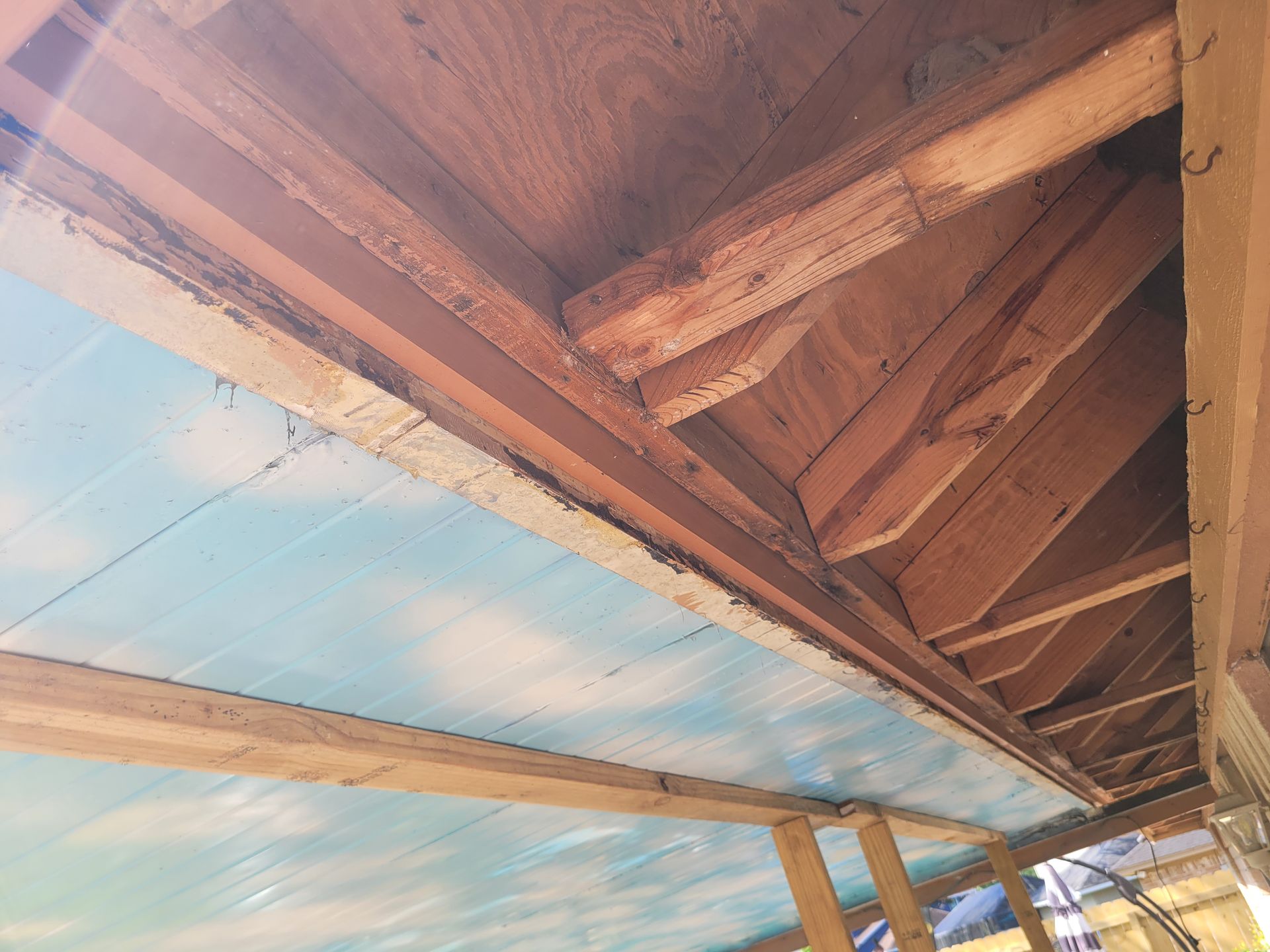 Wooden roof beams and blue sky seen from below a rustic porch ceiling