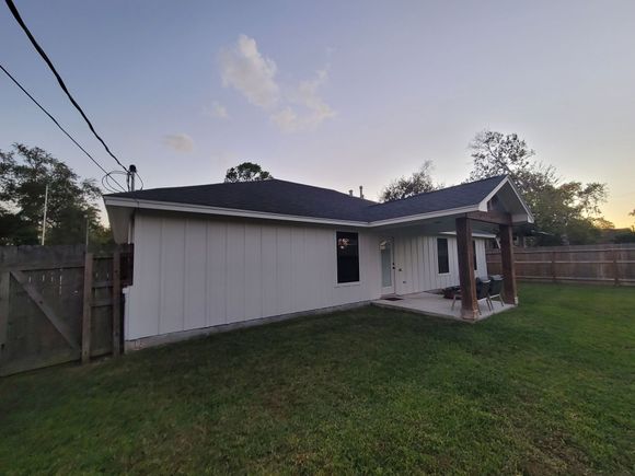 Small white house with a dark roof and fenced yard at sunset