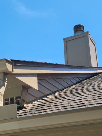 Rooftop with gray shingles, white chimney, and blue sky above.