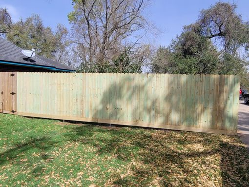 A long wooden fence spans a grassy yard with trees and a house in the background.