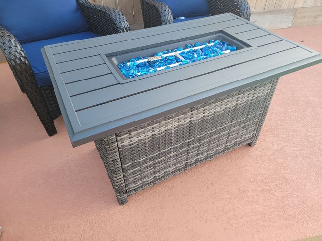 Outdoor wicker fire pit table with a blue flame in a patio seating area